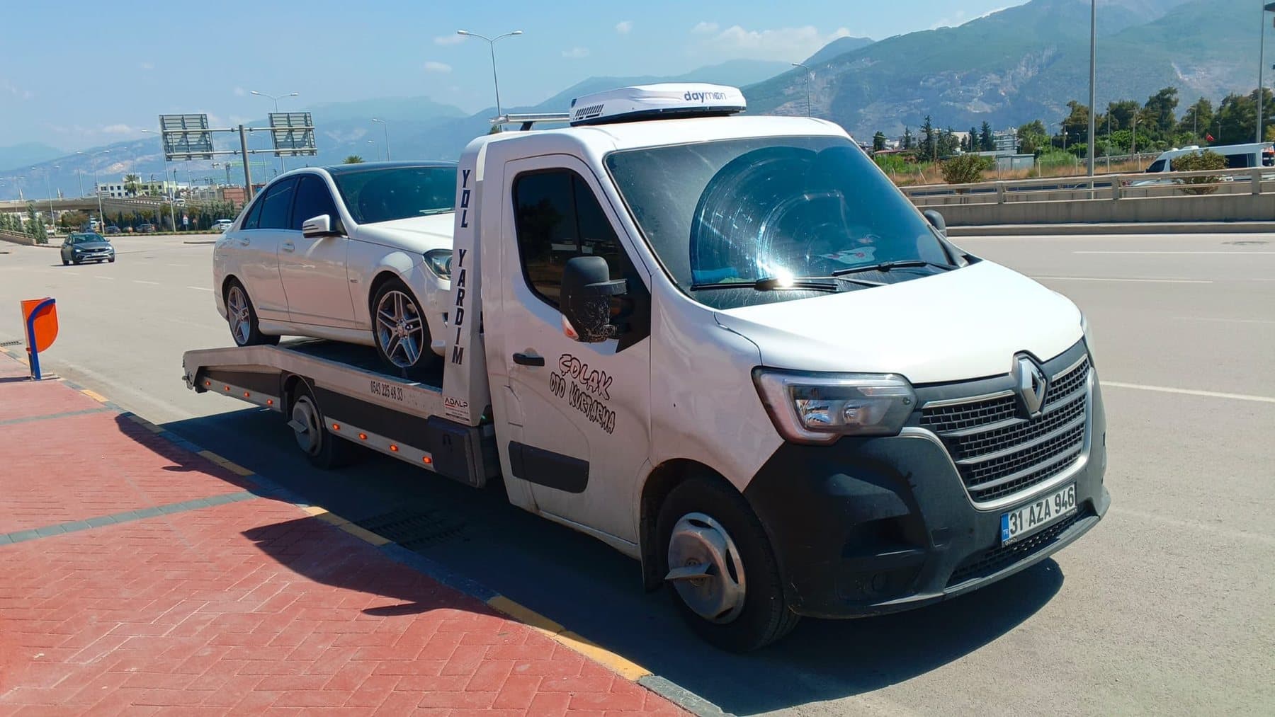 Dağ manzaralı yolda, kasasında beyaz sedan taşıyan Çolak Oto Kurtarma çekicisi