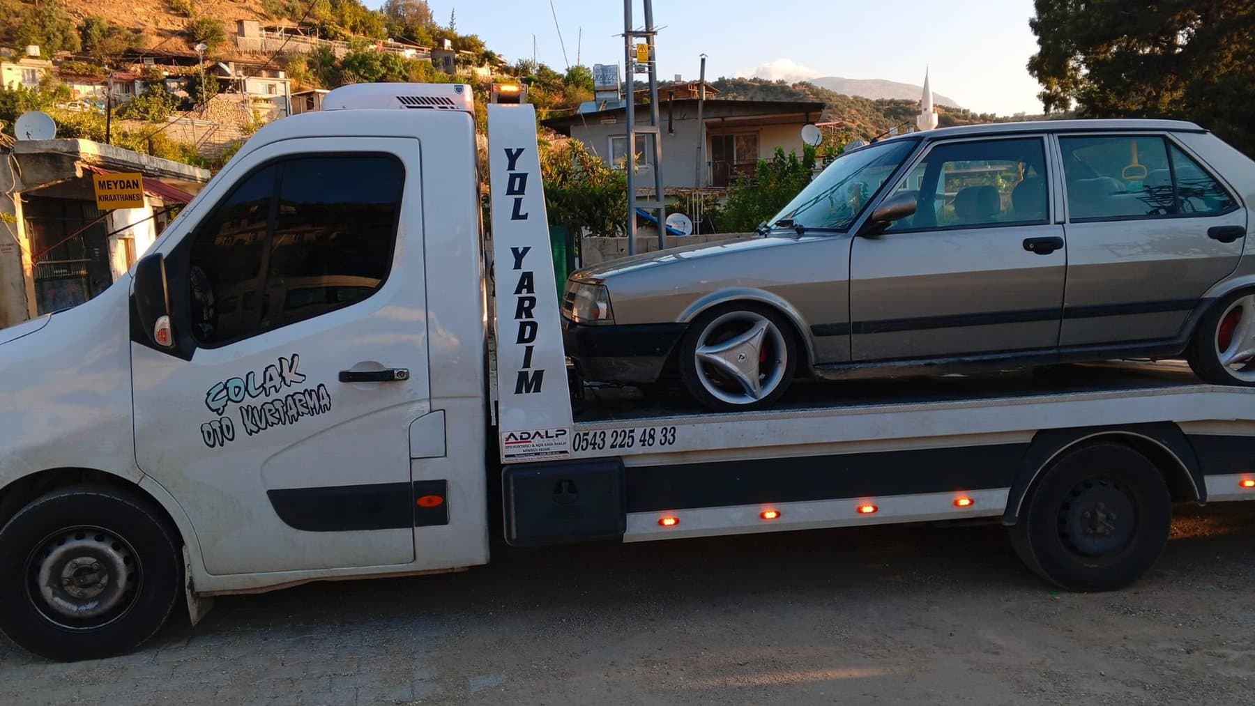 Köy içinde kasasında eski model otomobil taşıyan Çolak Oto Kurtarma çekicisi