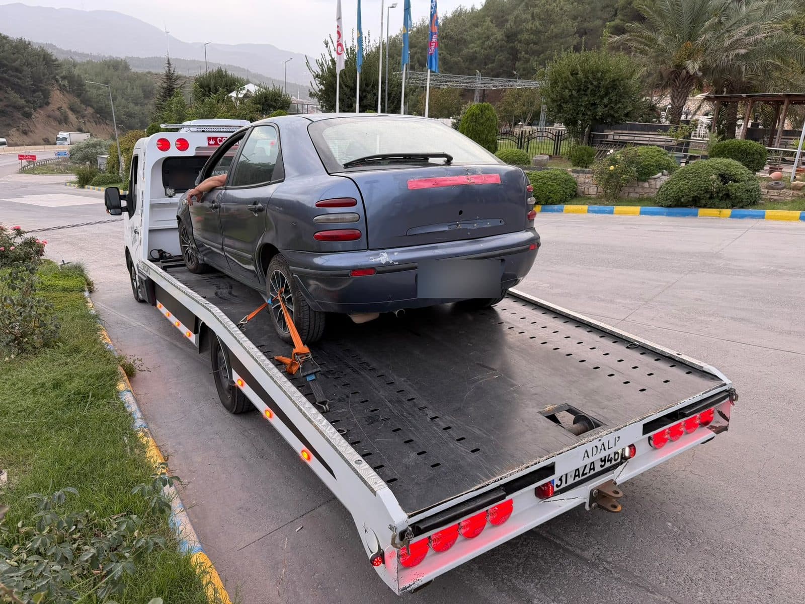 Çekici kasasında turuncu kayışlarla tekerleğinden bağlanmış lacivert otomobil