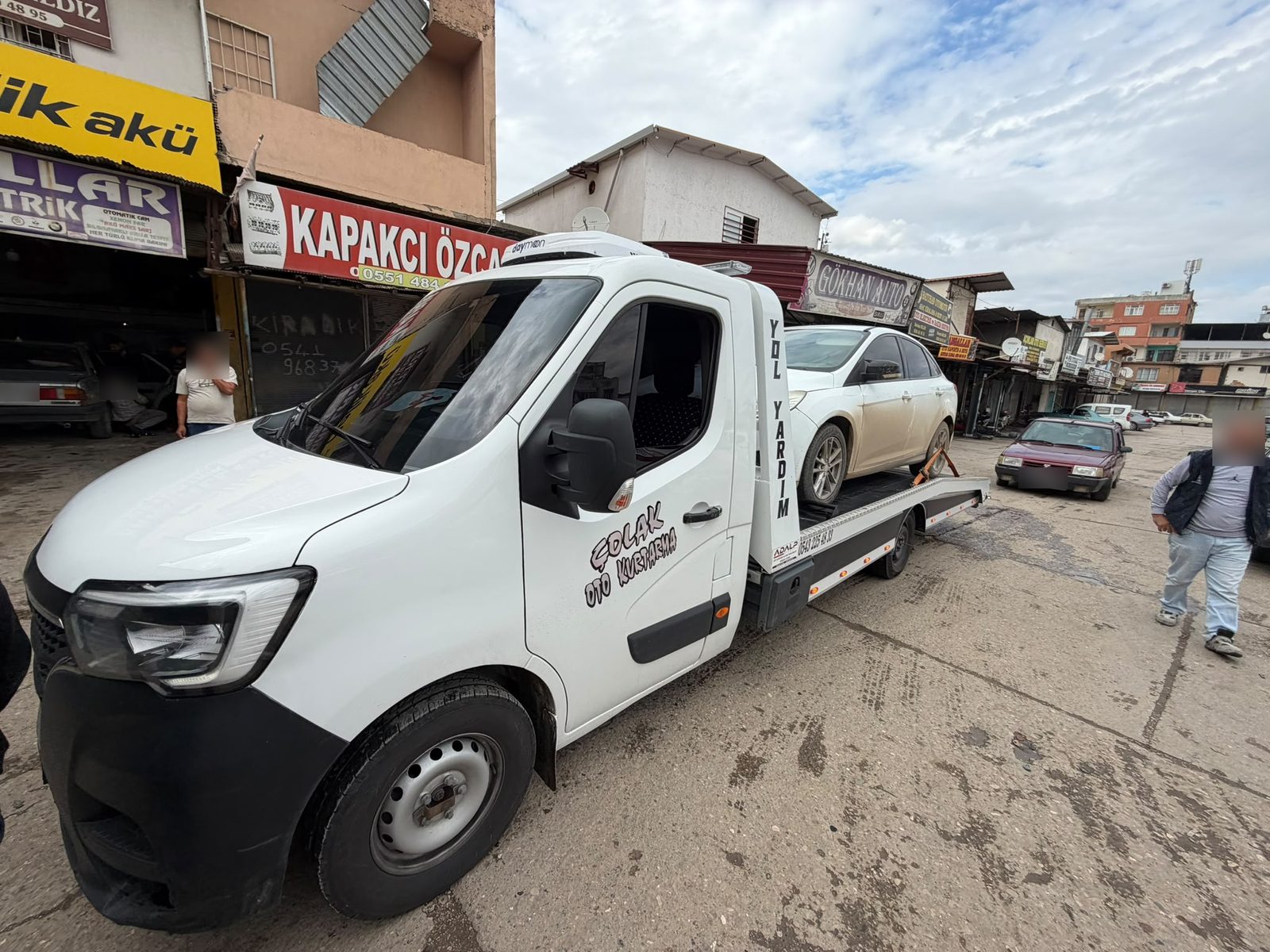 Sanayi sitesinde, kasasında beyaz sedan otomobil taşıyan Çolak Oto Kurtarma çekicisi
