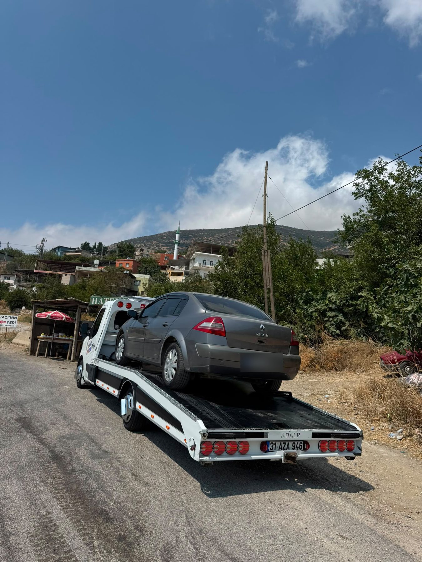 Köy yolunda kasasında gri sedan taşıyan Çolak Oto Kurtarma çekicisi, arkadan görünüş
